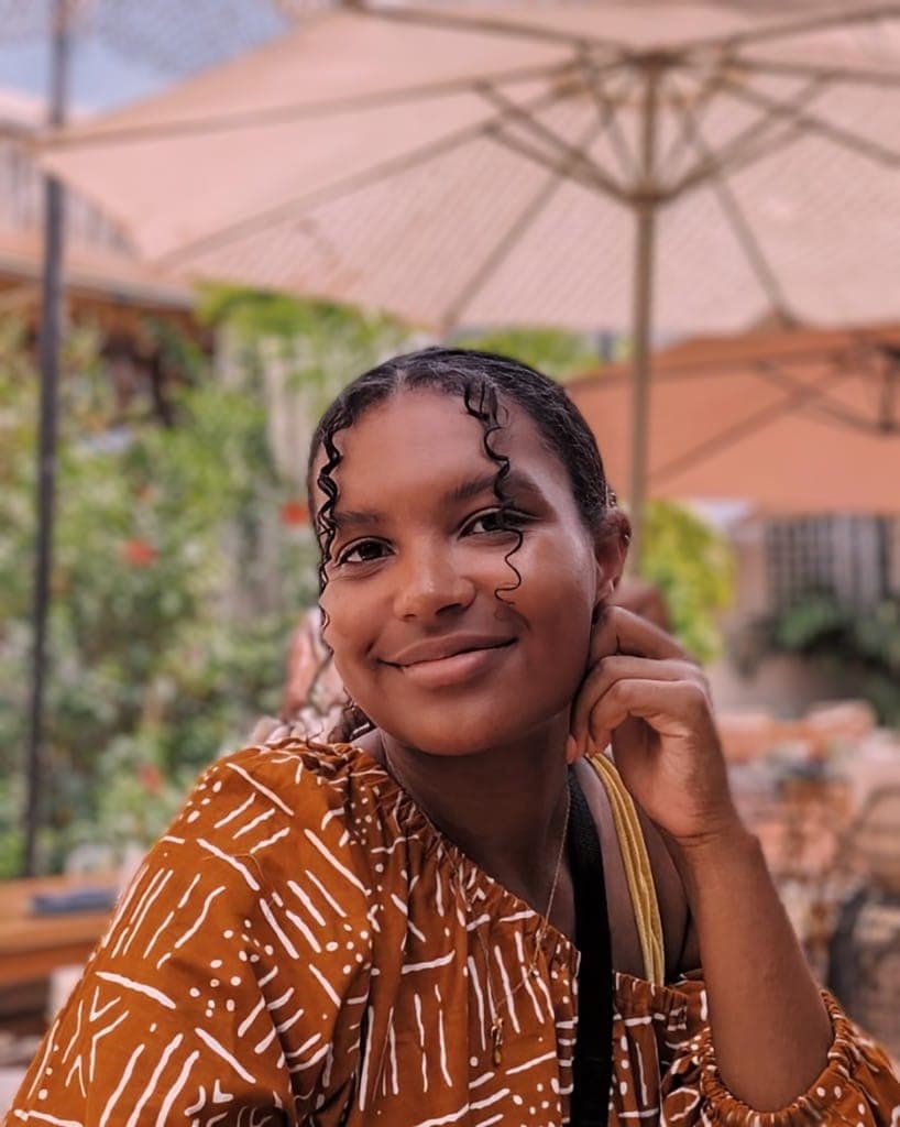 Kristel is a brown-skinned woman with curly dark hair. She is smiling with her head tilted to the left side.