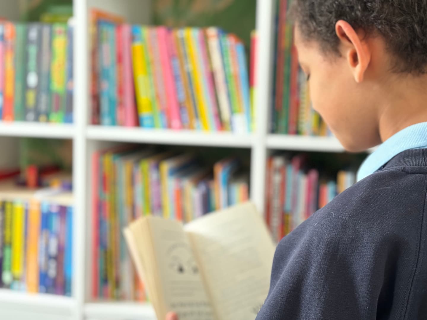 Schoolboy reading a book at home, library in the background